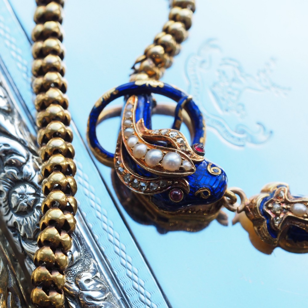 A Victorian 18-carat gold woven chain necklace featuring a blue enamel snake head set with seed pearls, small diamonds, and ruby eyes.