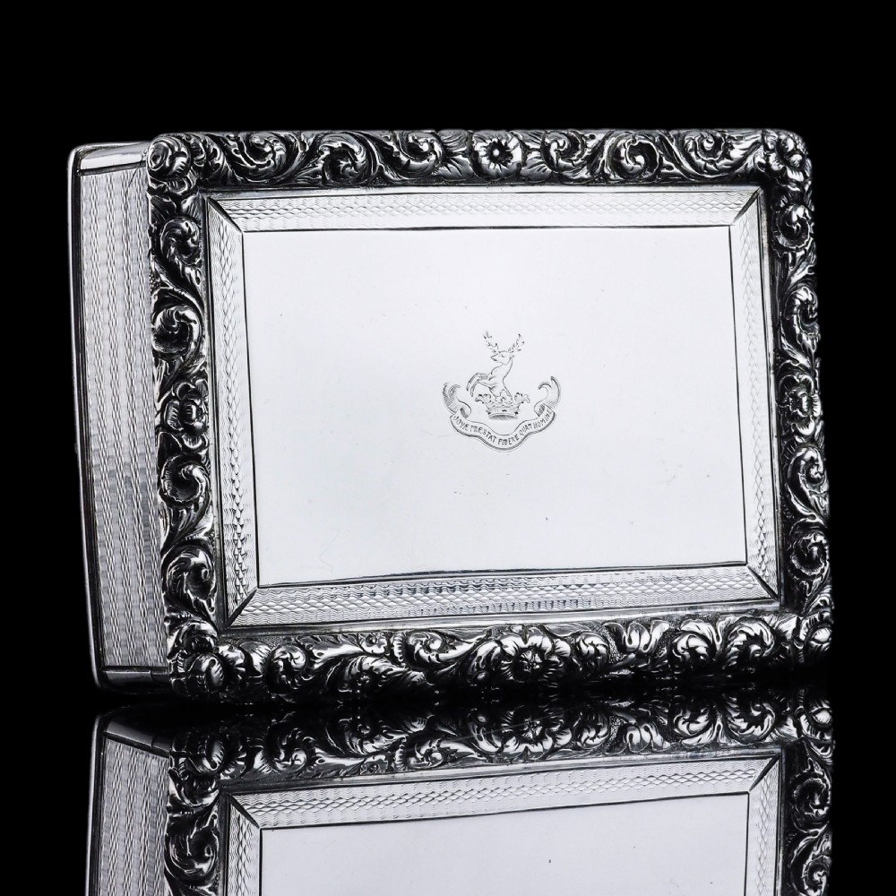 A rectangular sterling silver Georgian snuff box featuring a chased floral border, engine-turned detailing, and a central engraved crest. View II