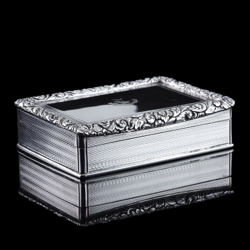 A rectangular sterling silver Georgian snuff box featuring a chased floral border, engine-turned detailing, and a central engraved crest. View IV