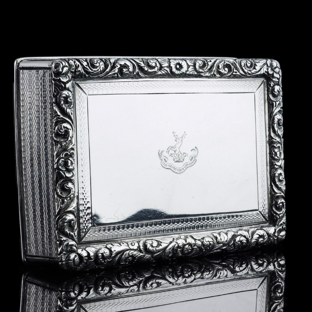 A rectangular sterling silver Georgian snuff box featuring a chased floral border, engine-turned detailing, and a central engraved crest.