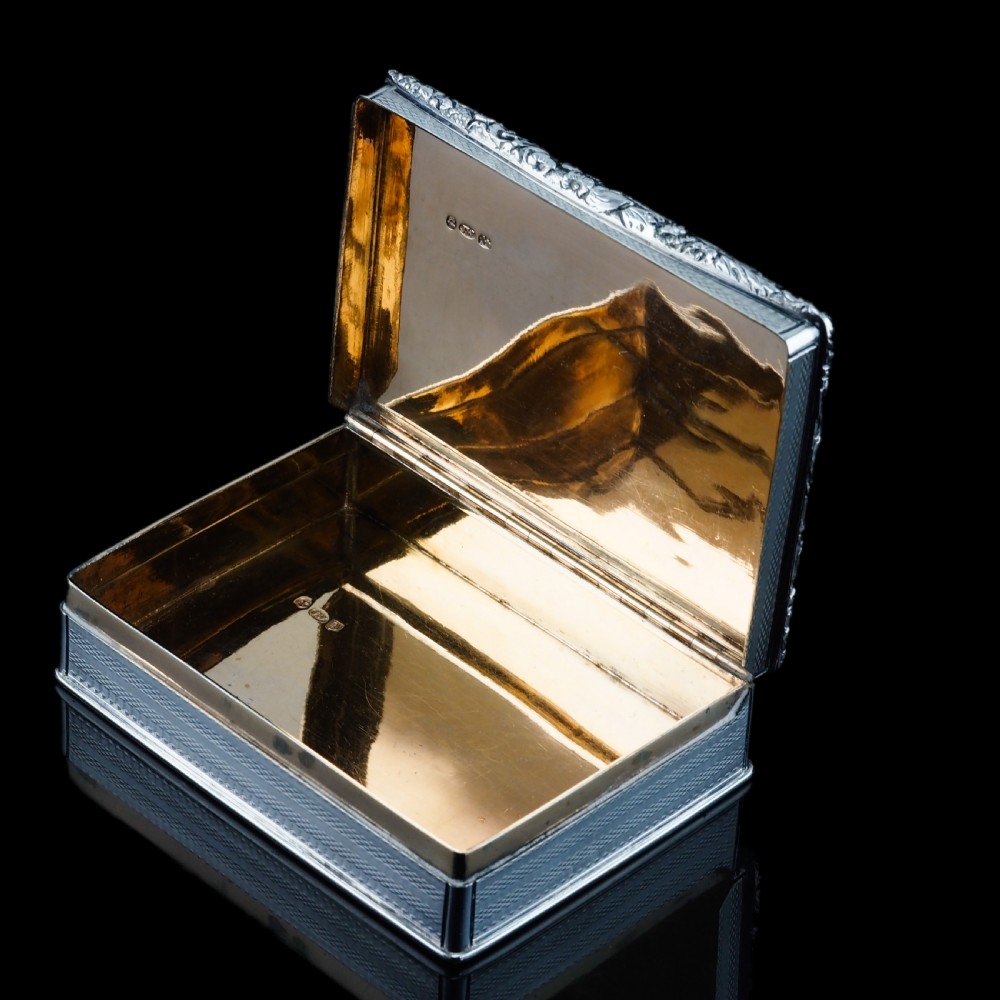 A rectangular sterling silver Georgian snuff box featuring a chased floral border, engine-turned detailing, and a central engraved crest. View IX