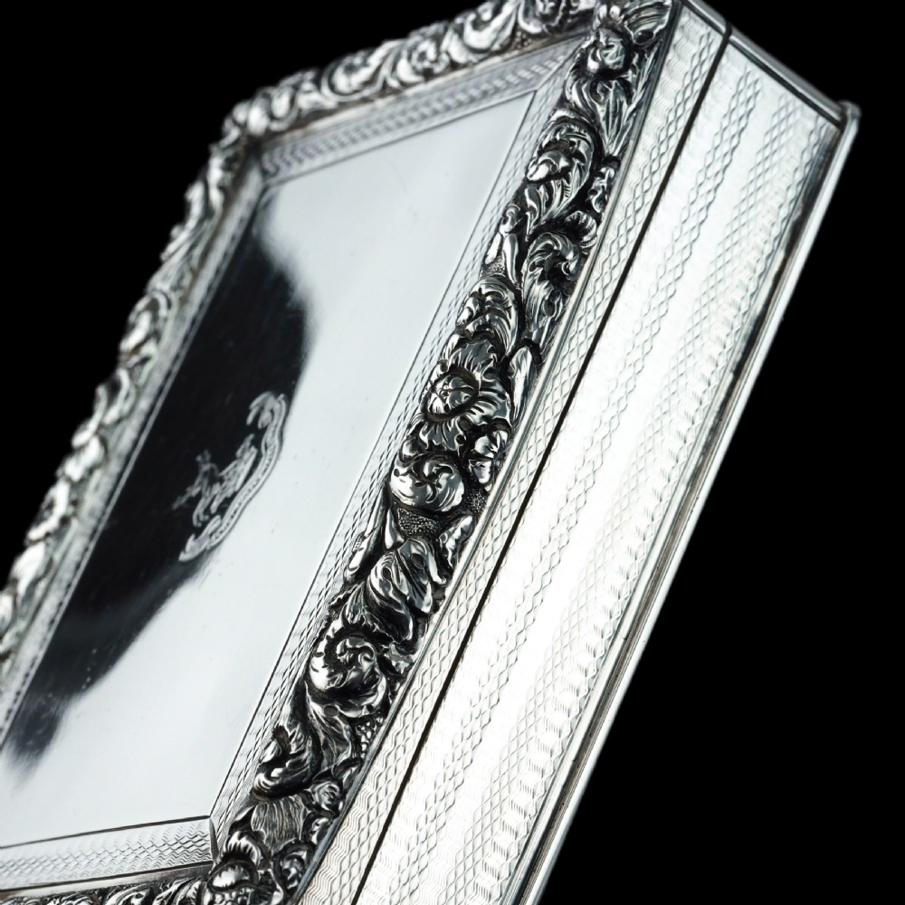 A rectangular sterling silver Georgian snuff box featuring a chased floral border, engine-turned detailing, and a central engraved crest. View XIII