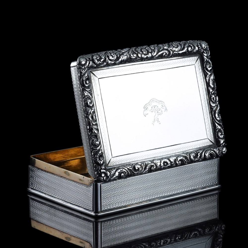 A rectangular sterling silver Georgian snuff box featuring a chased floral border, engine-turned detailing, and a central engraved crest. View XV