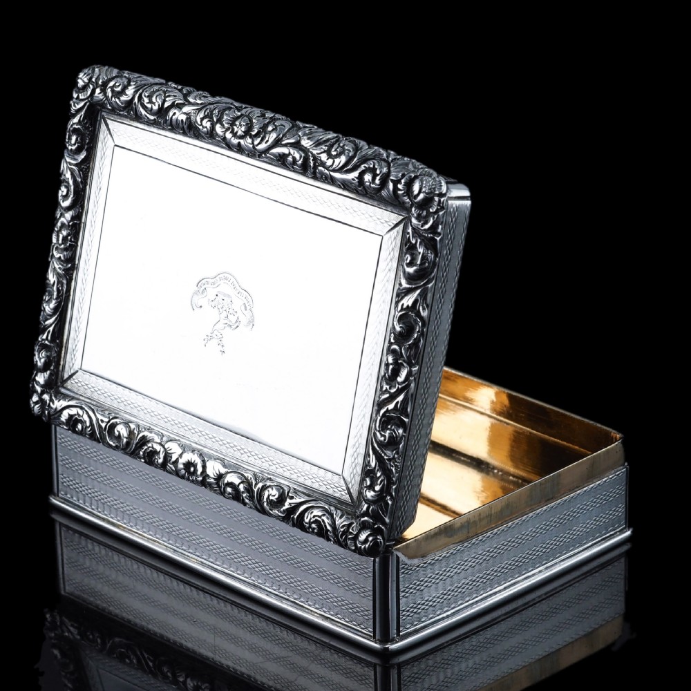 A rectangular sterling silver Georgian snuff box featuring a chased floral border, engine-turned detailing, and a central engraved crest. View XVI