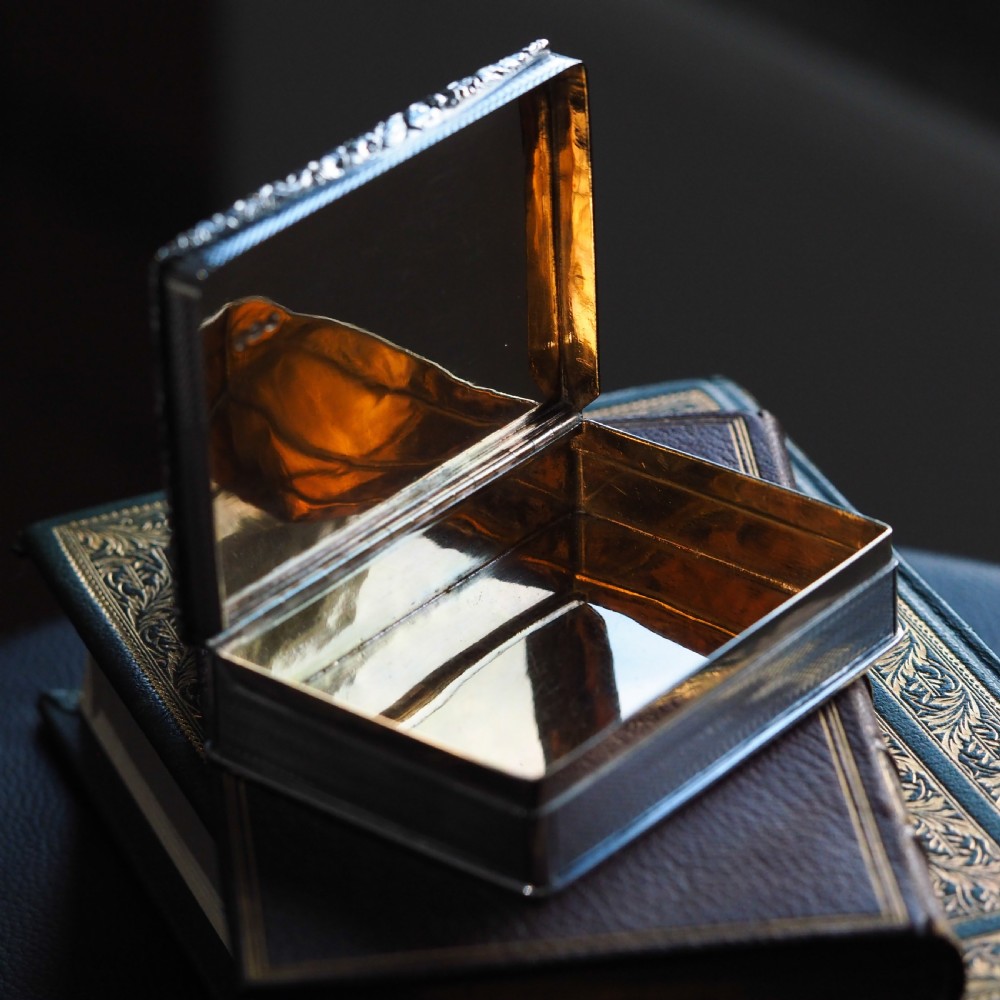 A rectangular sterling silver Georgian snuff box featuring a chased floral border, engine-turned detailing, and a central engraved crest. View XXI