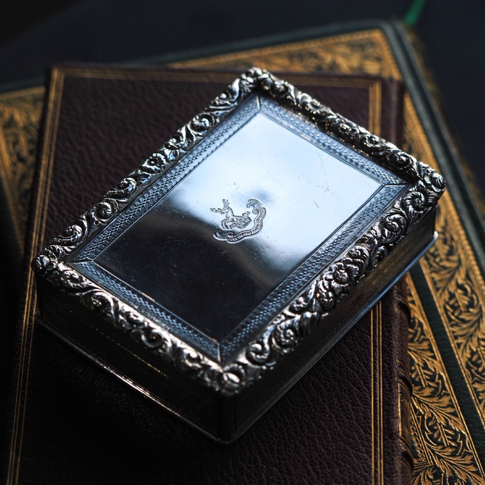A rectangular sterling silver Georgian snuff box featuring a chased floral border, engine-turned detailing, and a central engraved crest. View XXIII