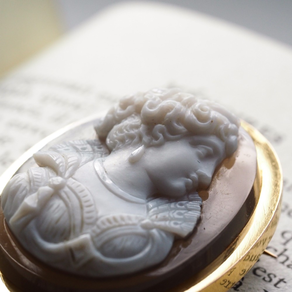 An oval Victorian hardstone agate cameo featuring a white relief carved portrait of a woman against a dark background, set in a plain 18ct gold bezel frame. View V