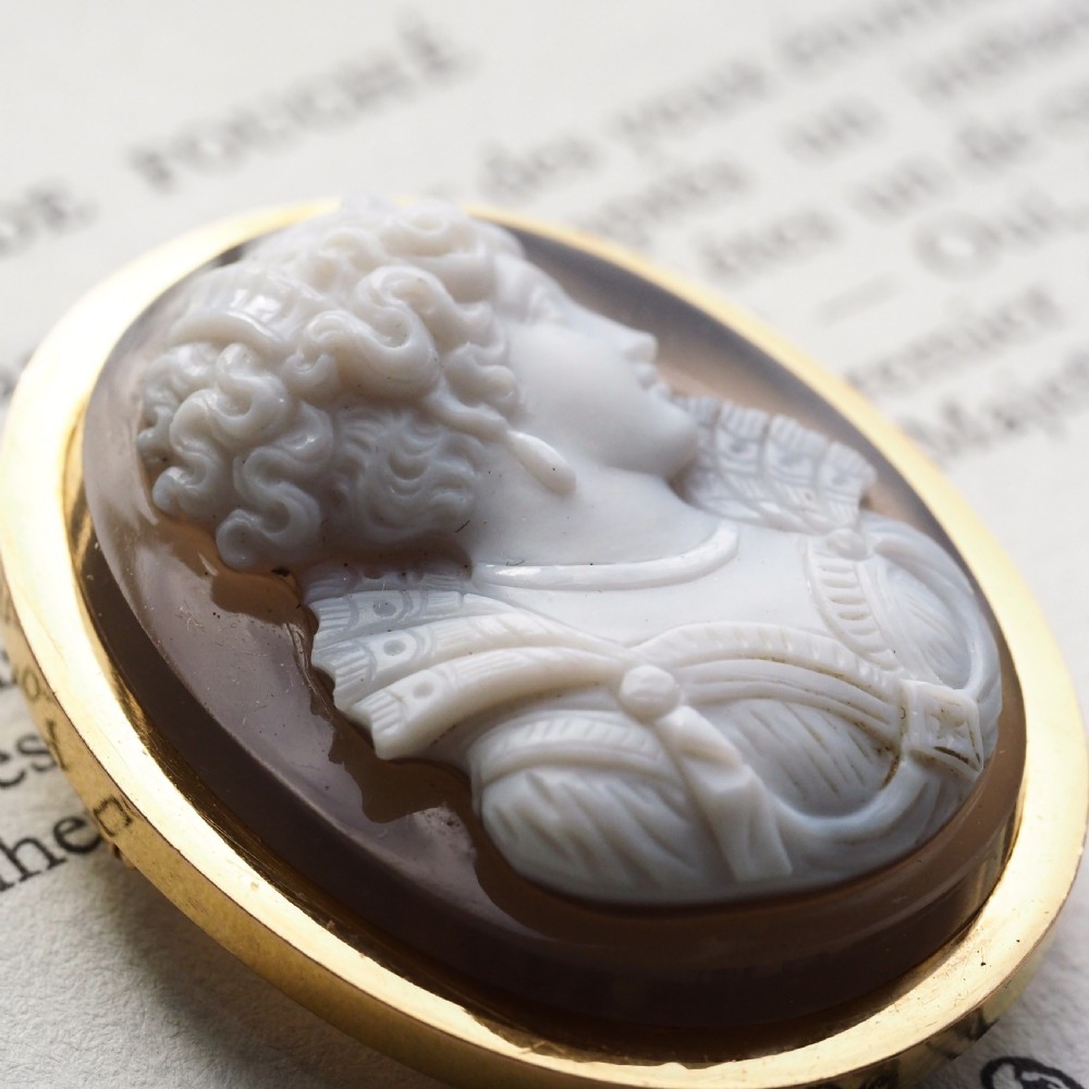 An oval Victorian hardstone agate cameo featuring a white relief carved portrait of a woman against a dark background, set in a plain 18ct gold bezel frame. View VI