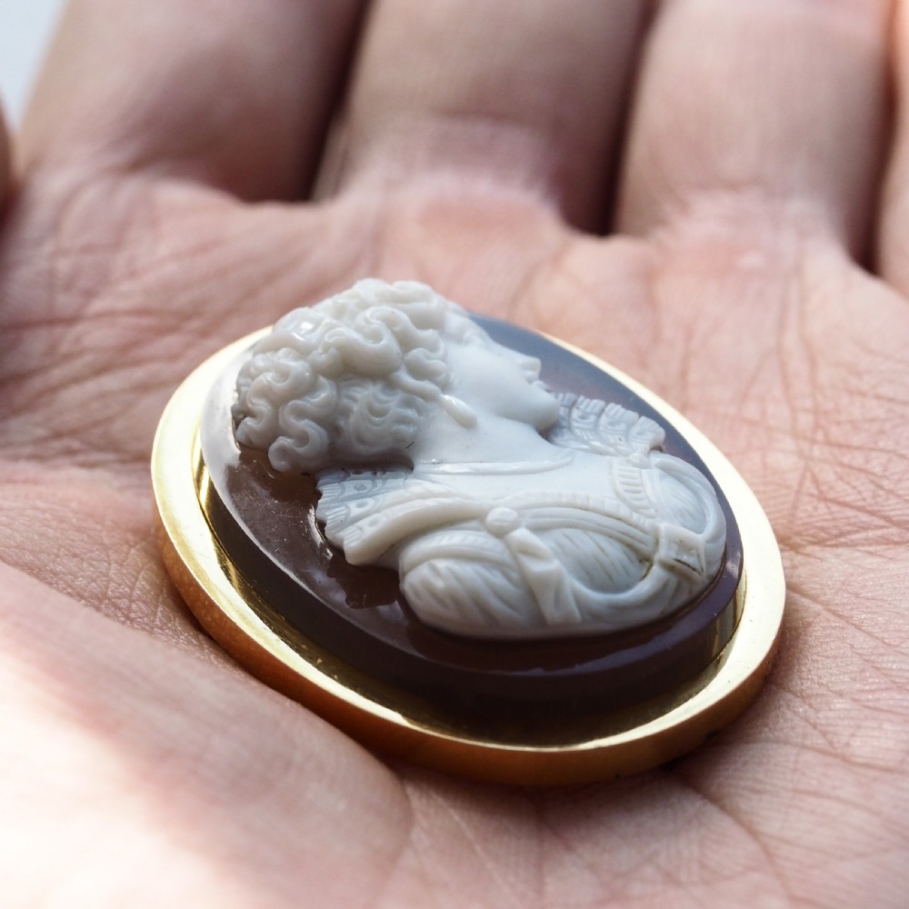 An oval Victorian hardstone agate cameo featuring a white relief carved portrait of a woman against a dark background, set in a plain 18ct gold bezel frame. View XV