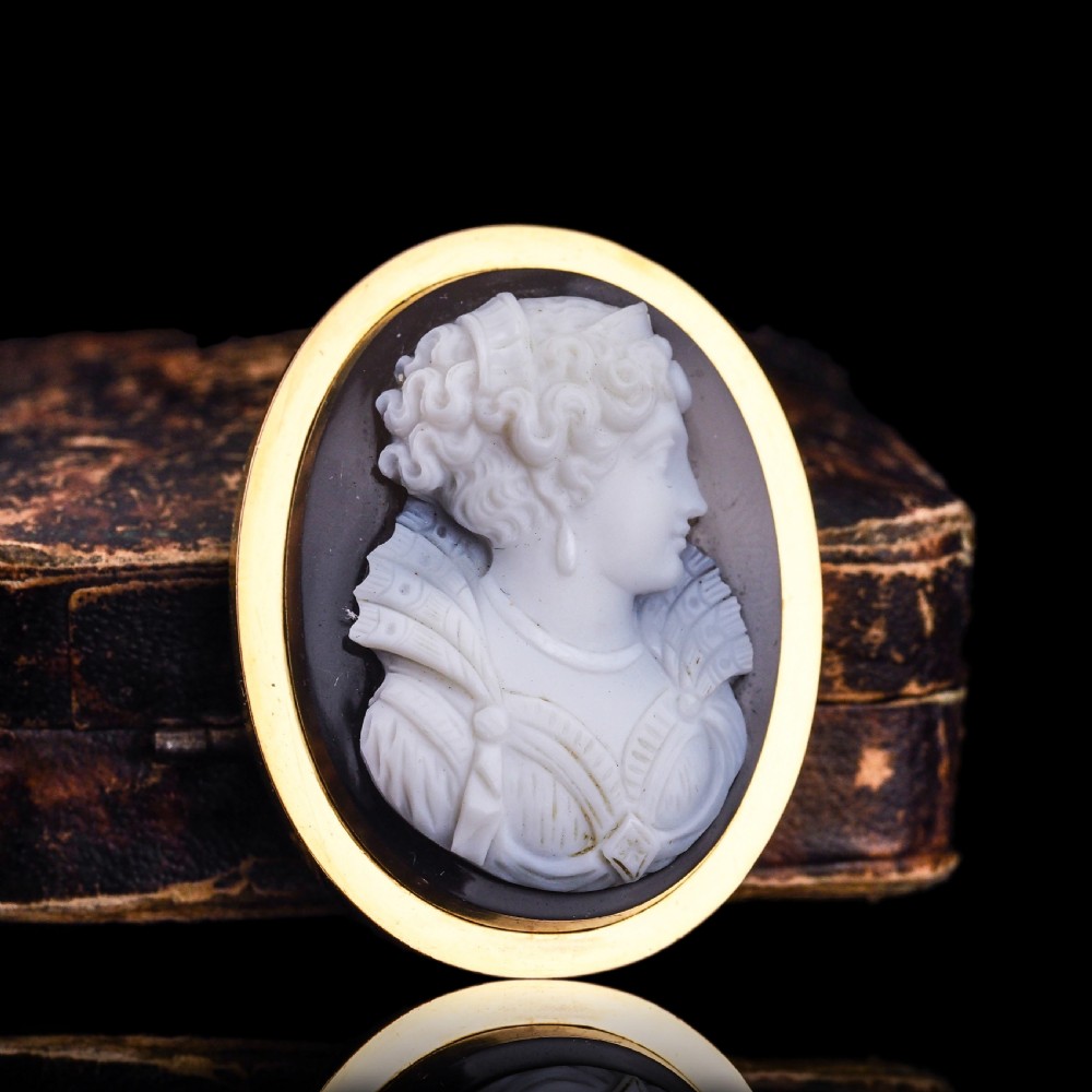 An oval Victorian hardstone agate cameo featuring a white relief carved portrait of a woman against a dark background, set in a plain 18ct gold bezel frame. View XVI