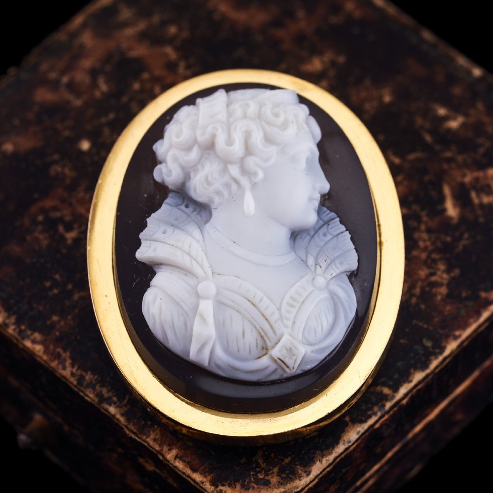 An oval Victorian hardstone agate cameo featuring a white relief carved portrait of a woman against a dark background, set in a plain 18ct gold bezel frame. View XIX