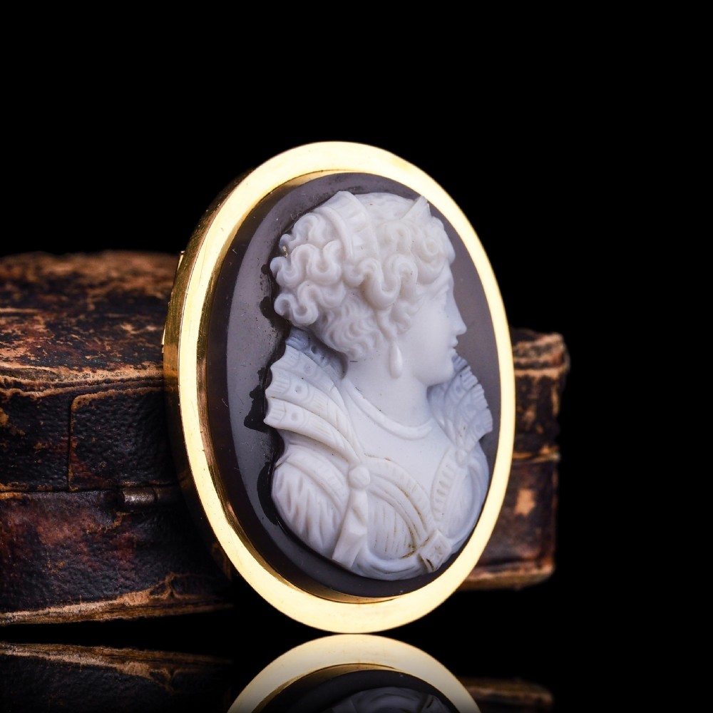 An oval Victorian hardstone agate cameo featuring a white relief carved portrait of a woman against a dark background, set in a plain 18ct gold bezel frame. View XX