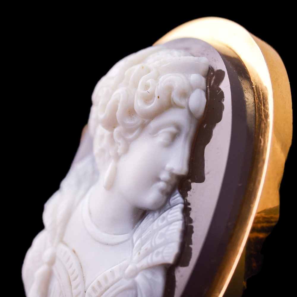 An oval Victorian hardstone agate cameo featuring a white relief carved portrait of a woman against a dark background, set in a plain 18ct gold bezel frame. View XXV