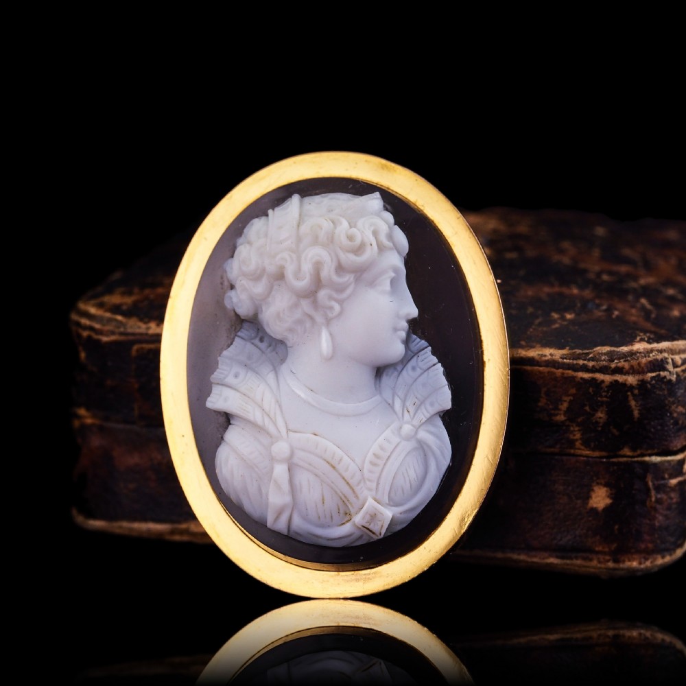 An oval Victorian hardstone agate cameo featuring a white relief carved portrait of a woman against a dark background, set in a plain 18ct gold bezel frame. View XXVI