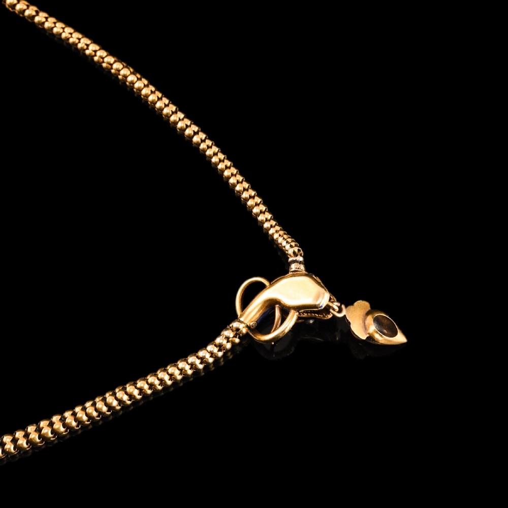 An antique Victorian 18-carat gold snake necklace featuring a flexible chain and a blue enamel serpent head decorated with seed pearls and diamonds. View X