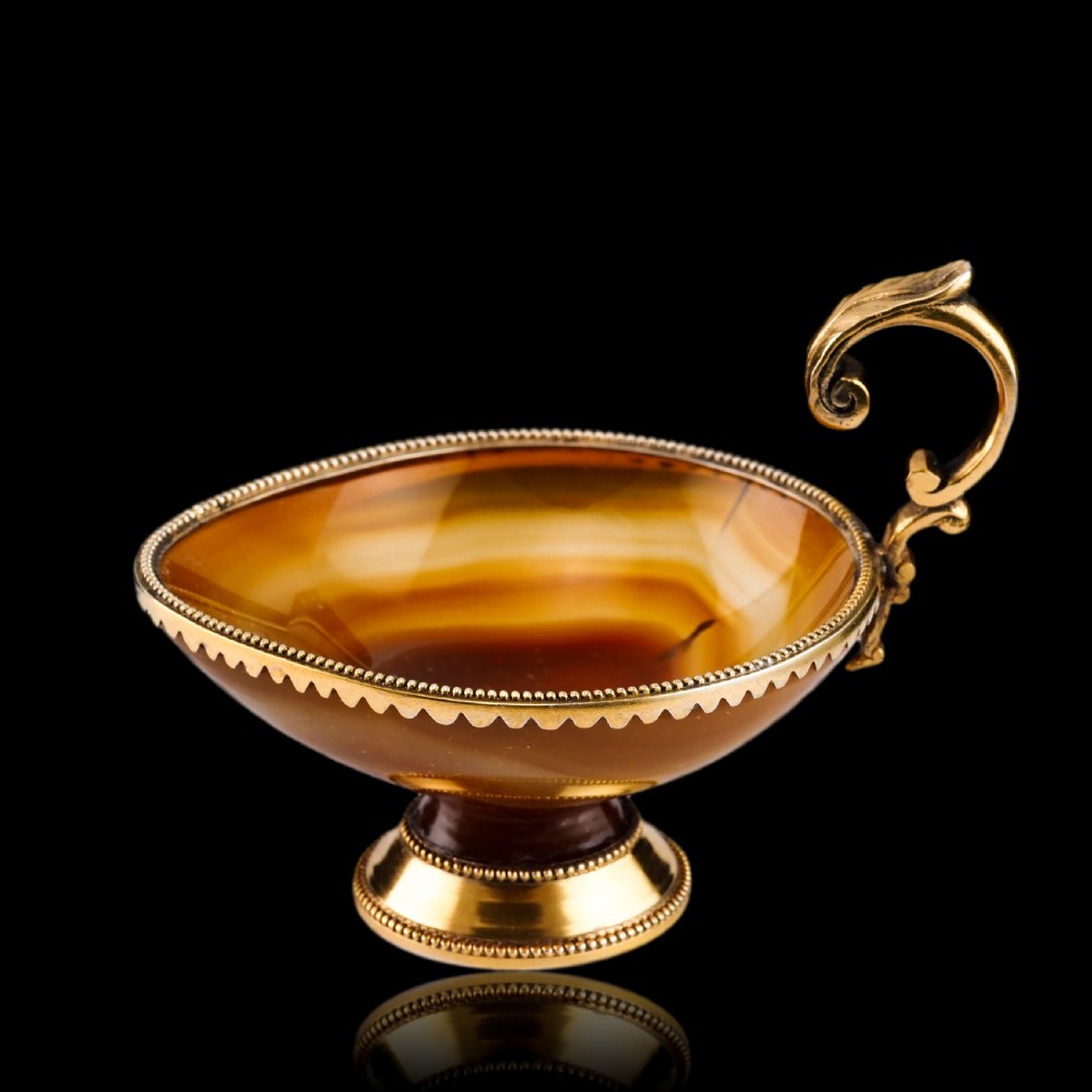 A 19th-century carved brown banded agate cup featuring a silver-gilt rim, pedestal base, and an ornate scroll handle. View VI