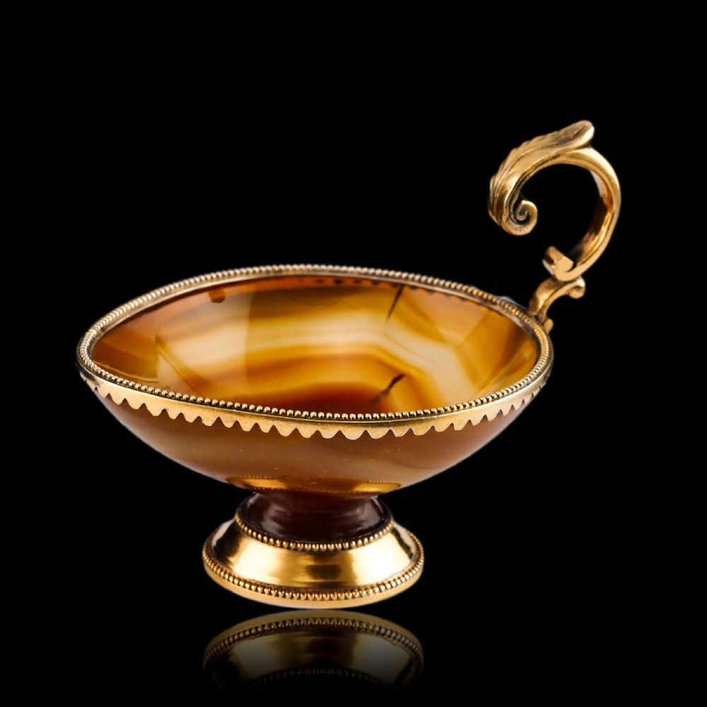 A 19th-century carved brown banded agate cup featuring a silver-gilt rim, pedestal base, and an ornate scroll handle. View VII