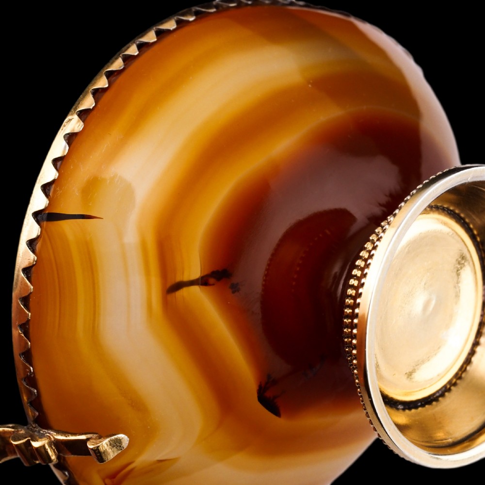 A 19th-century carved brown banded agate cup featuring a silver-gilt rim, pedestal base, and an ornate scroll handle. View X