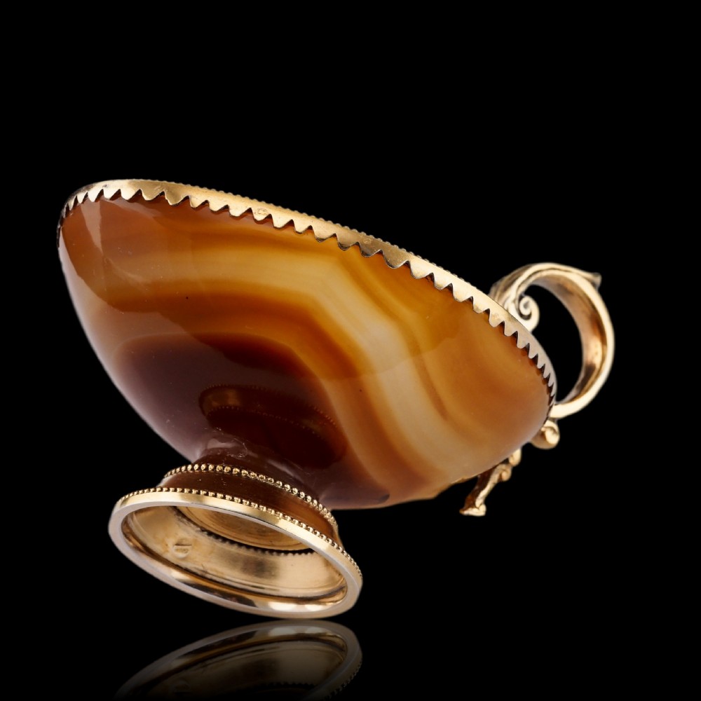 A 19th-century carved brown banded agate cup featuring a silver-gilt rim, pedestal base, and an ornate scroll handle. View XII