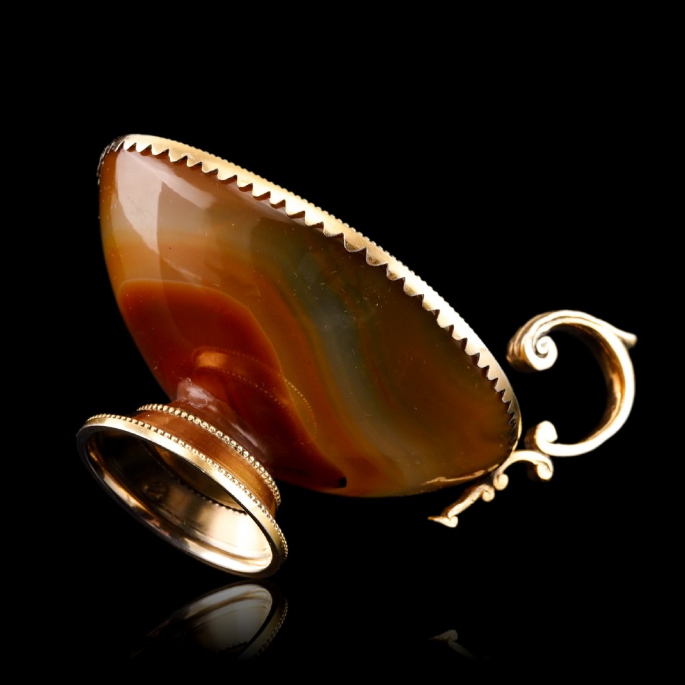 A 19th-century carved brown banded agate cup featuring a silver-gilt rim, pedestal base, and an ornate scroll handle. View XIV
