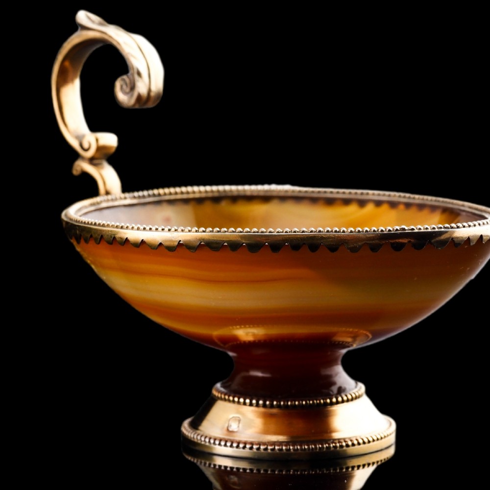 A 19th-century carved brown banded agate cup featuring a silver-gilt rim, pedestal base, and an ornate scroll handle. View XV