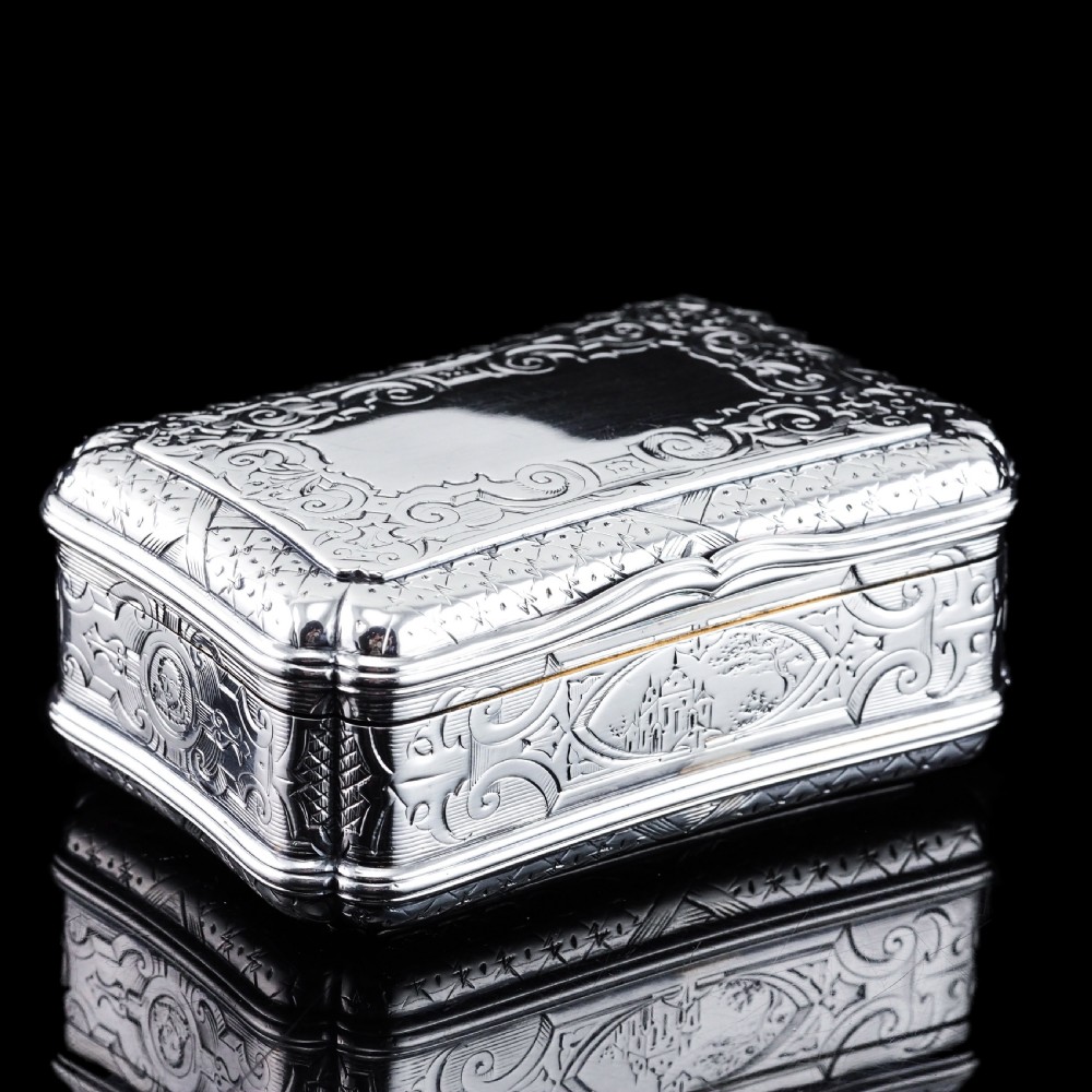 A Victorian sterling silver table snuff box with shaped cartouche outlines, foliage engraving, and an architectural scene.