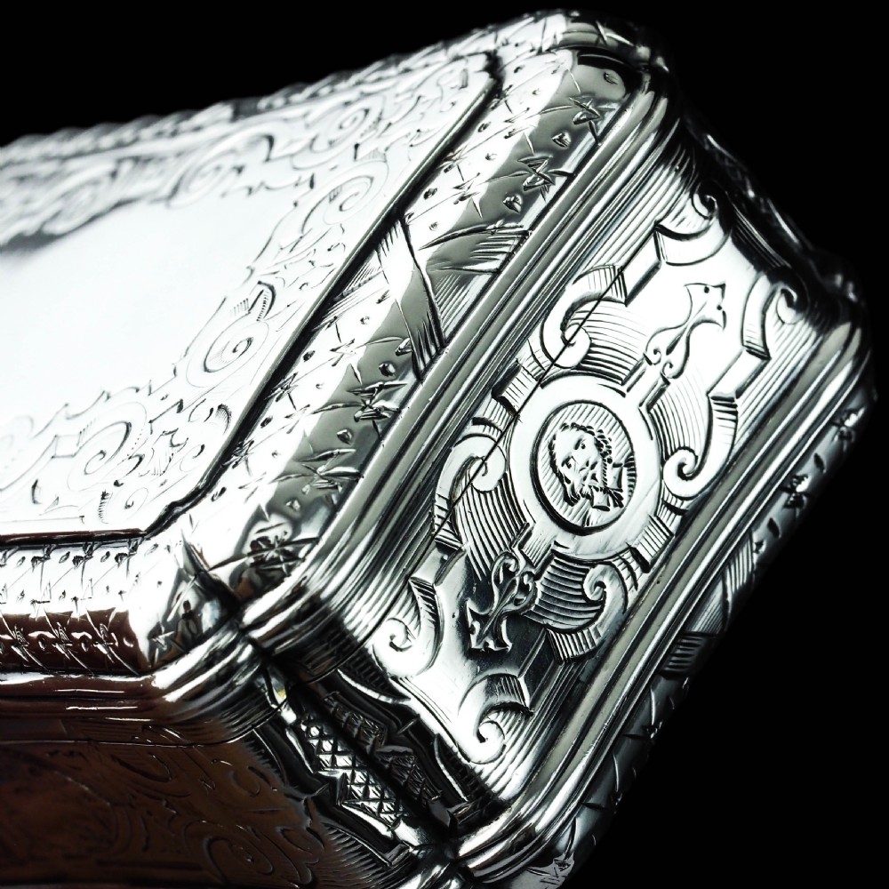 A Victorian sterling silver table snuff box with shaped cartouche outlines, foliage engraving, and an architectural scene. View II