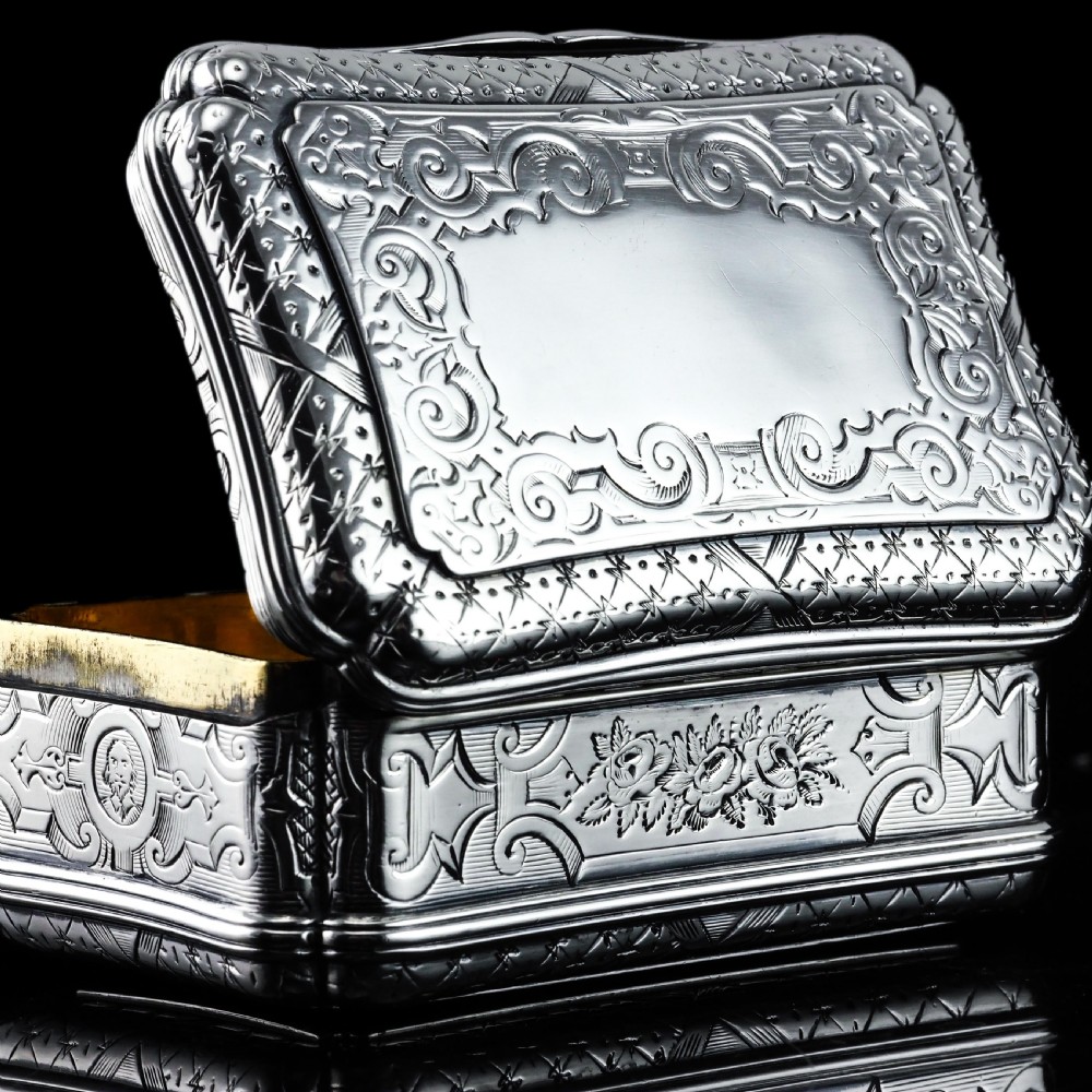 A Victorian sterling silver table snuff box with shaped cartouche outlines, foliage engraving, and an architectural scene. View IX