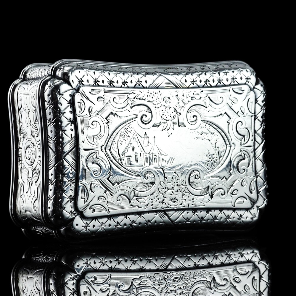 A Victorian sterling silver table snuff box with shaped cartouche outlines, foliage engraving, and an architectural scene. View XI