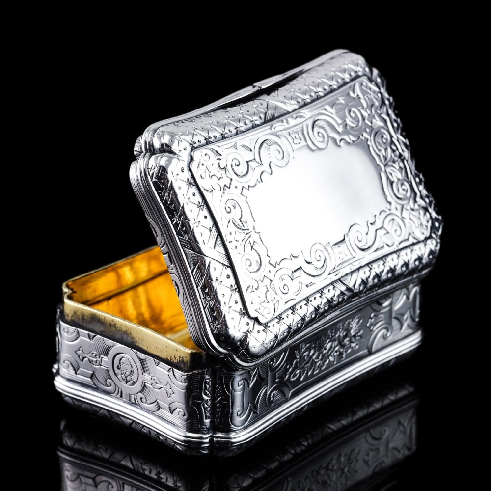 A Victorian sterling silver table snuff box with shaped cartouche outlines, foliage engraving, and an architectural scene. View XVI