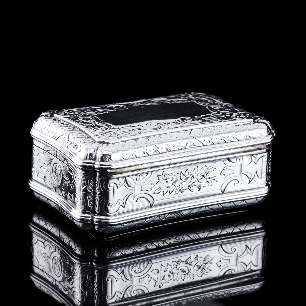 A Victorian sterling silver table snuff box with shaped cartouche outlines, foliage engraving, and an architectural scene. View XVII