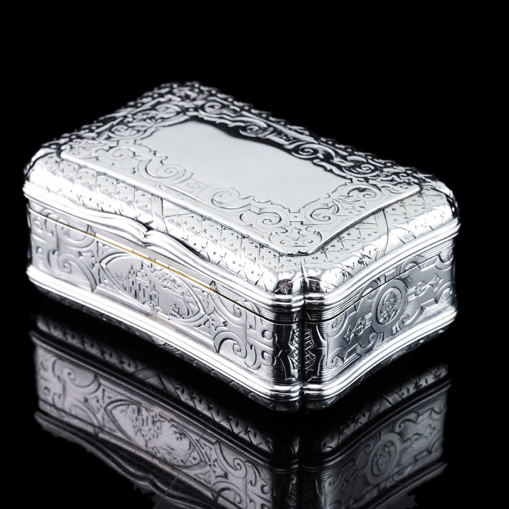 A Victorian sterling silver table snuff box with shaped cartouche outlines, foliage engraving, and an architectural scene. View XVIII