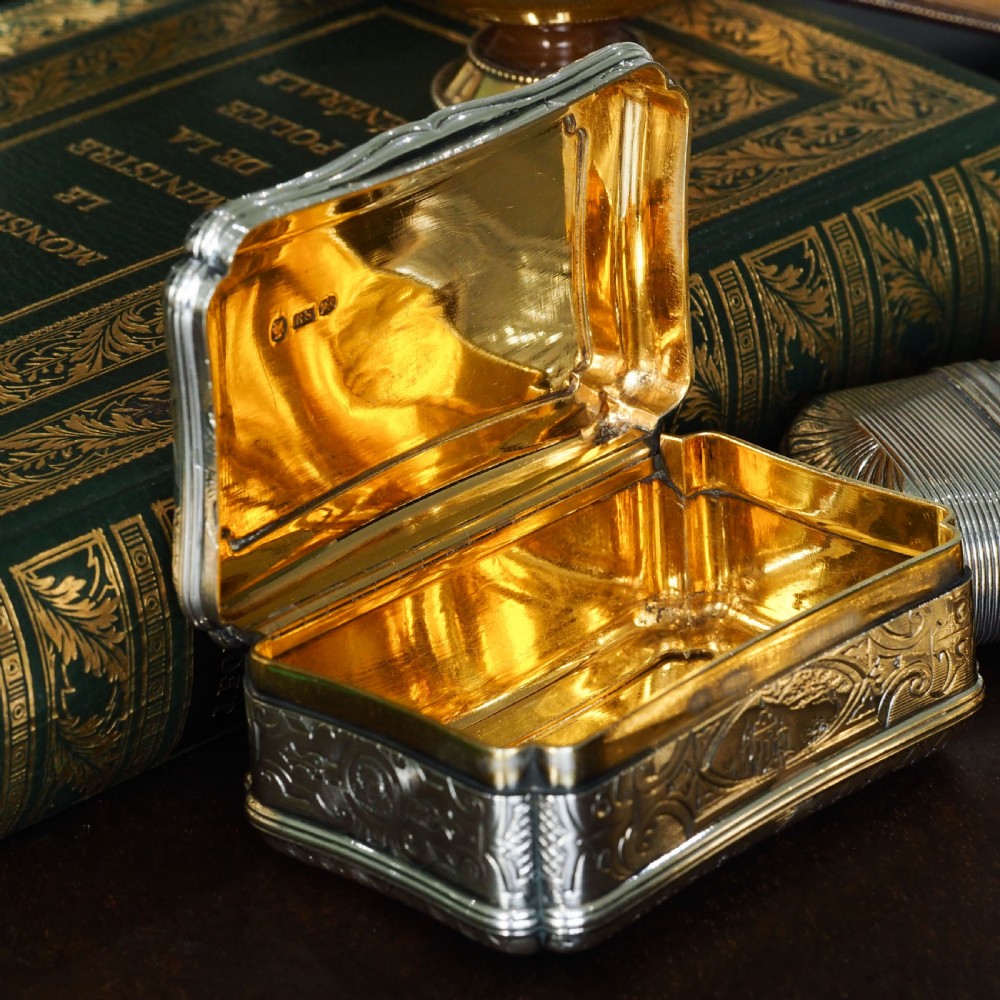A Victorian sterling silver table snuff box with shaped cartouche outlines, foliage engraving, and an architectural scene. View XIX