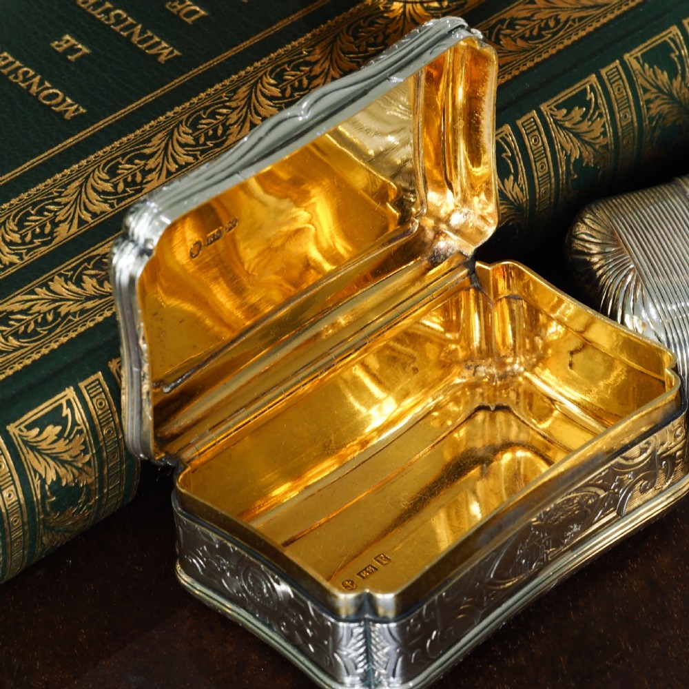A Victorian sterling silver table snuff box with shaped cartouche outlines, foliage engraving, and an architectural scene. View XXI