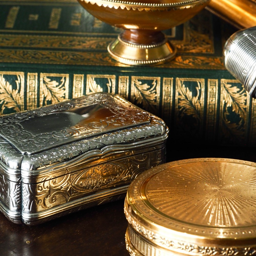 A Victorian sterling silver table snuff box with shaped cartouche outlines, foliage engraving, and an architectural scene. View XXIV