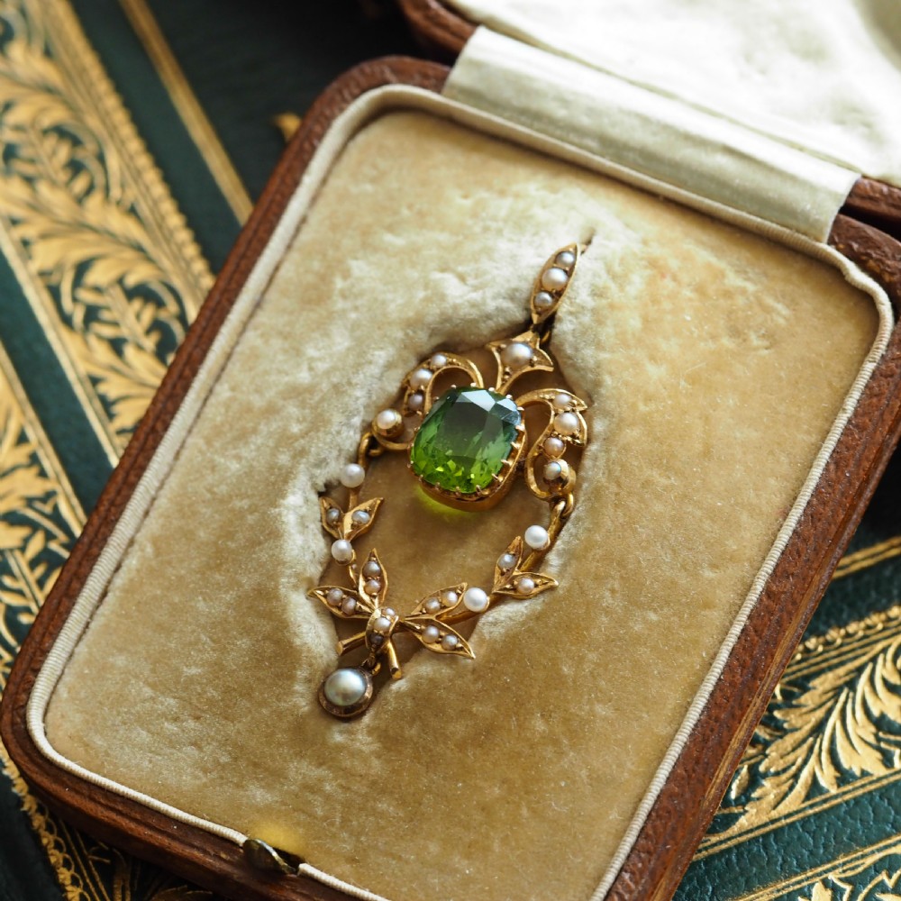 A late Victorian 14-carat yellow gold openwork pendant featuring a cushion-cut green peridot encircled by seed pearl foliate scrolls and a dangling pearl drop. View V