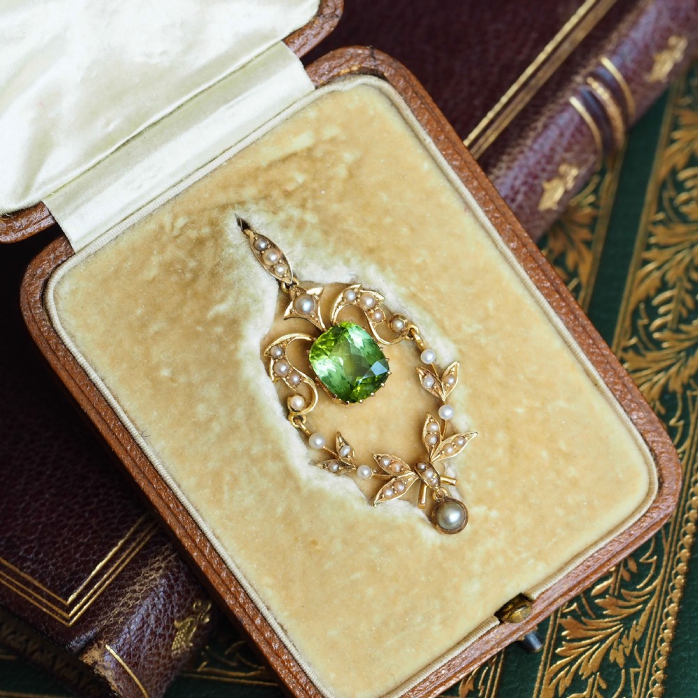 A late Victorian 14-carat yellow gold openwork pendant featuring a cushion-cut green peridot encircled by seed pearl foliate scrolls and a dangling pearl drop. View VI
