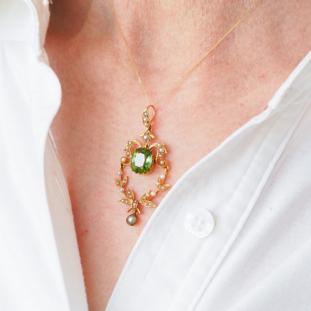 A late Victorian 14-carat yellow gold openwork pendant featuring a cushion-cut green peridot encircled by seed pearl foliate scrolls and a dangling pearl drop. View XII