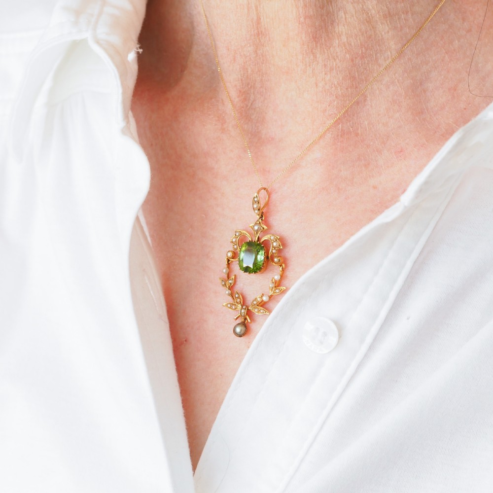 A late Victorian 14-carat yellow gold openwork pendant featuring a cushion-cut green peridot encircled by seed pearl foliate scrolls and a dangling pearl drop. View XIII