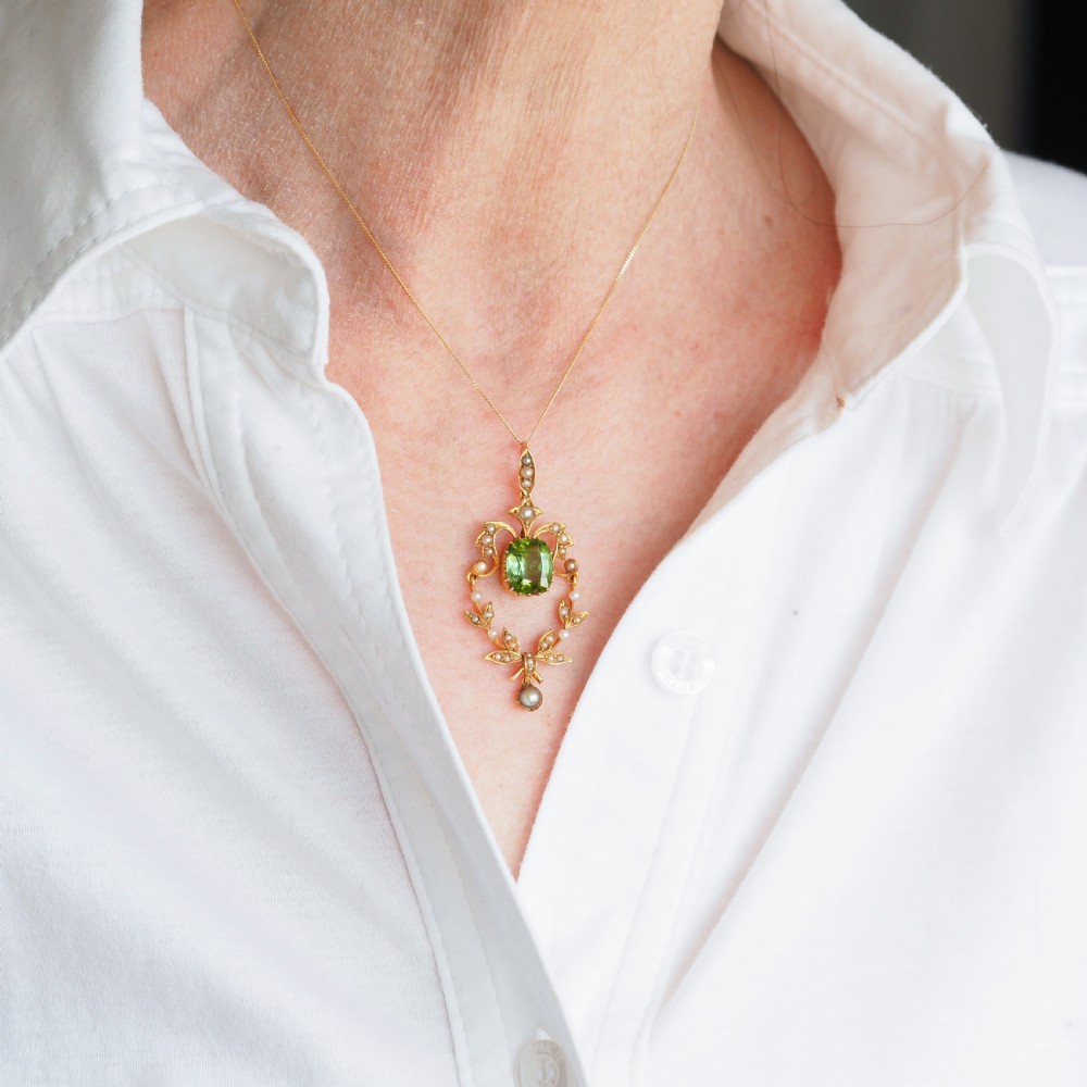A late Victorian 14-carat yellow gold openwork pendant featuring a cushion-cut green peridot encircled by seed pearl foliate scrolls and a dangling pearl drop. View XIV
