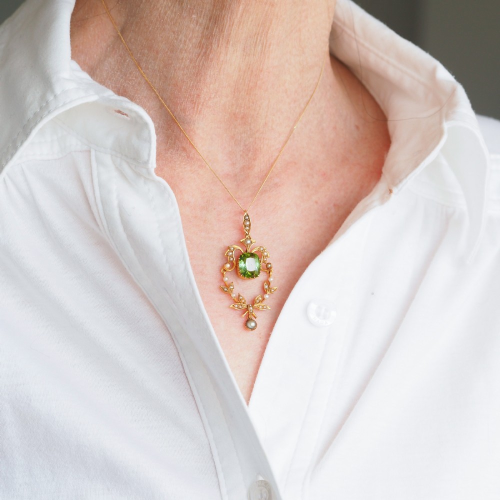 A late Victorian 14-carat yellow gold openwork pendant featuring a cushion-cut green peridot encircled by seed pearl foliate scrolls and a dangling pearl drop. View XV