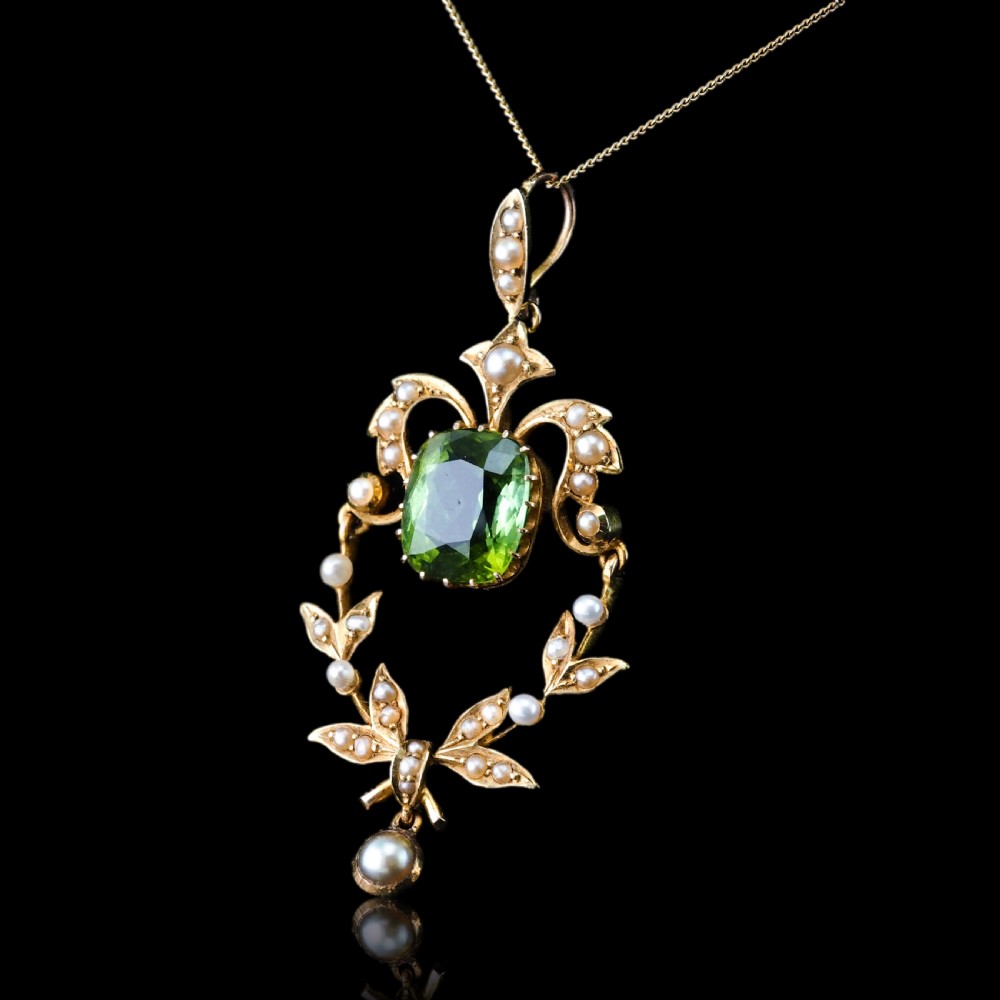 A late Victorian 14-carat yellow gold openwork pendant featuring a cushion-cut green peridot encircled by seed pearl foliate scrolls and a dangling pearl drop. View XIX