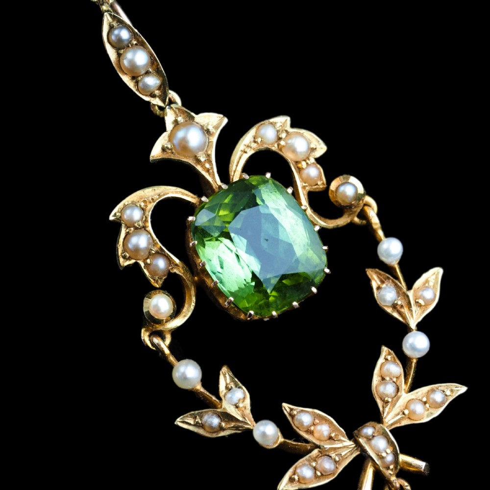 A late Victorian 14-carat yellow gold openwork pendant featuring a cushion-cut green peridot encircled by seed pearl foliate scrolls and a dangling pearl drop. View XXIII