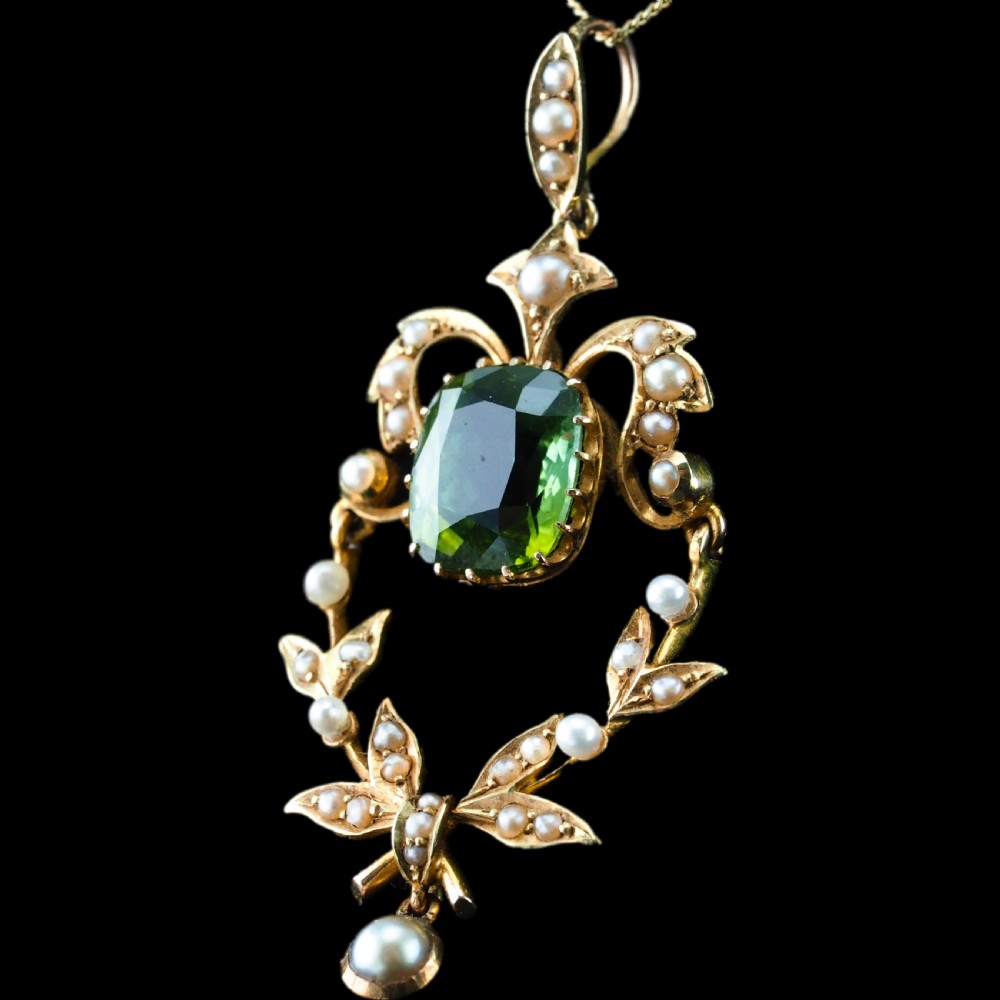 A late Victorian 14-carat yellow gold openwork pendant featuring a cushion-cut green peridot encircled by seed pearl foliate scrolls and a dangling pearl drop. View XXIV