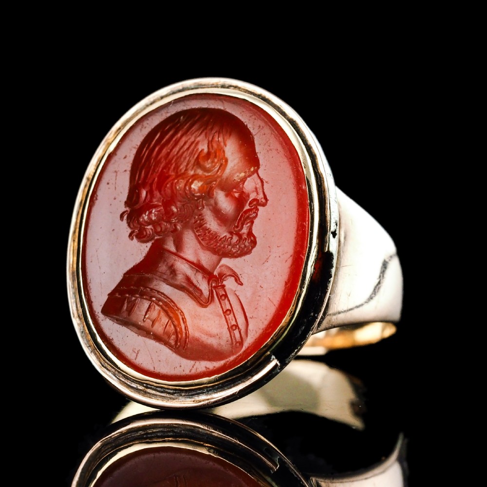 An antique gold signet ring featuring an oval red carnelian gemstone carved with the side profile portrait of a gentleman.