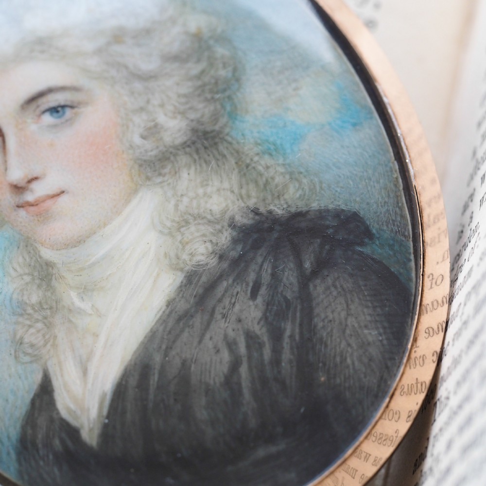 An oval Georgian portrait miniature depicting a subject with light powdered hair set in a 14k gold frame with a top bail. View VI
