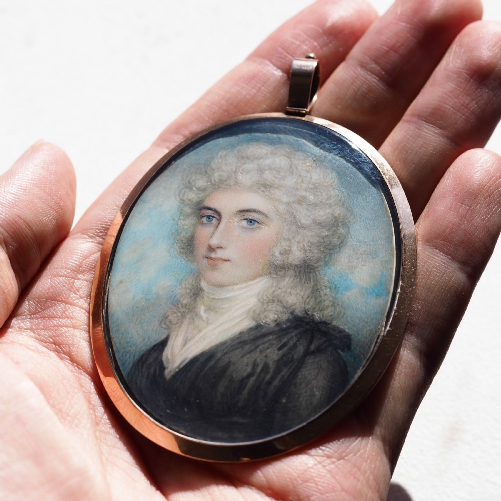 An oval Georgian portrait miniature depicting a subject with light powdered hair set in a 14k gold frame with a top bail. View X