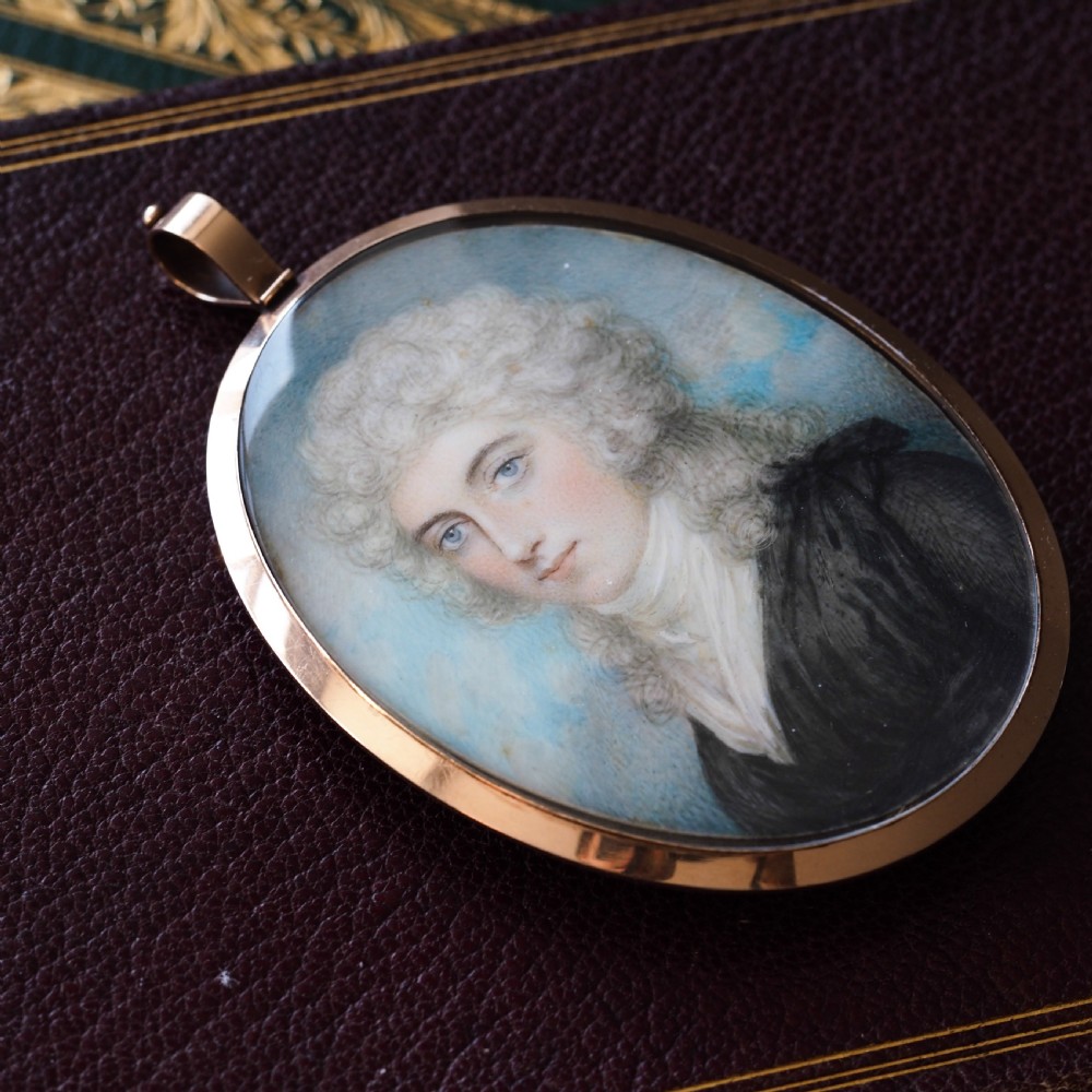 An oval Georgian portrait miniature depicting a subject with light powdered hair set in a 14k gold frame with a top bail. View XII