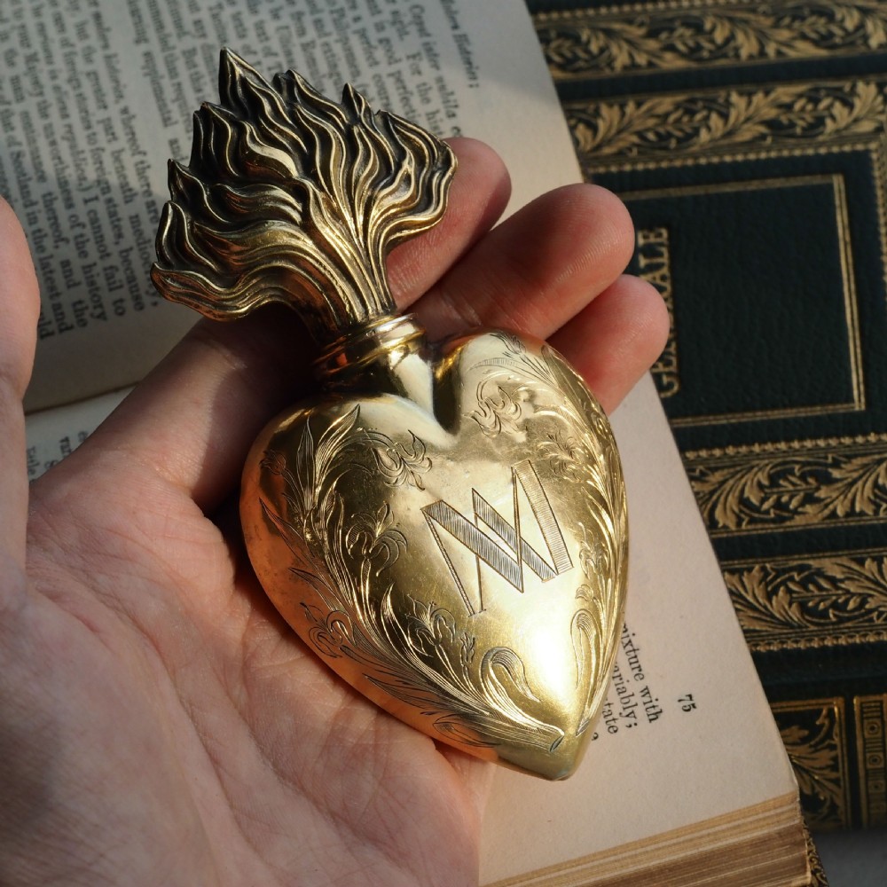 A 19th-century French silver-gilt heart-shaped scent bottle featuring an engraved monogram, foliate scrollwork, and a flame-shaped stopper. View V