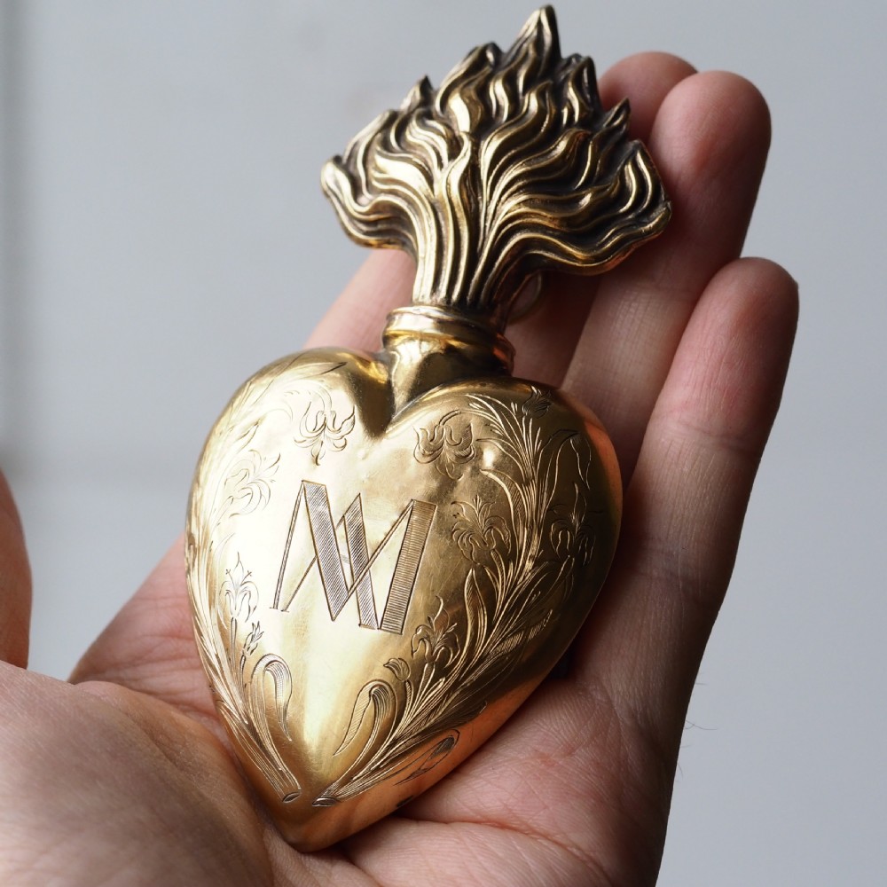 A 19th-century French silver-gilt heart-shaped scent bottle featuring an engraved monogram, foliate scrollwork, and a flame-shaped stopper. View X